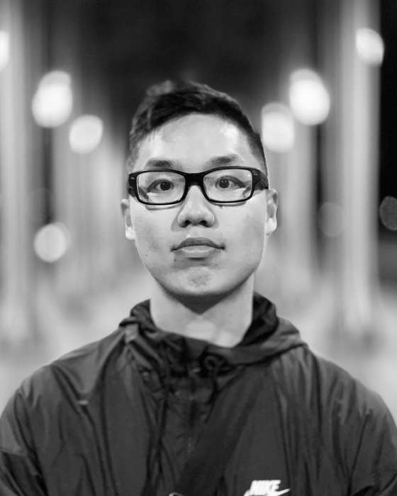Black and white portrait of David T Phung, wearing glasses and a zip jacket